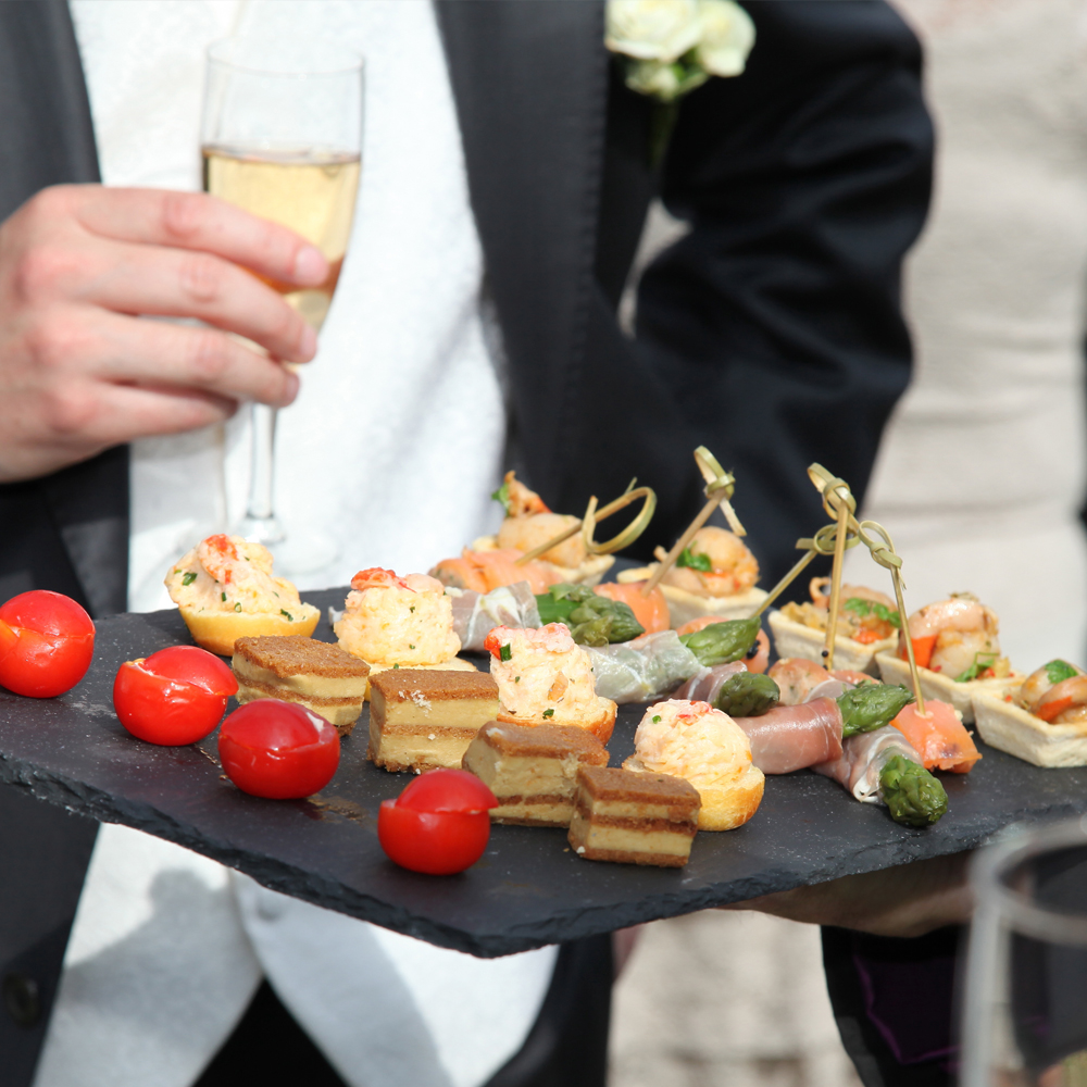 Kellner präsentiert Canapés auf Schieferplatte beim Catering Kromberg Hochzeitscatering in NRW.